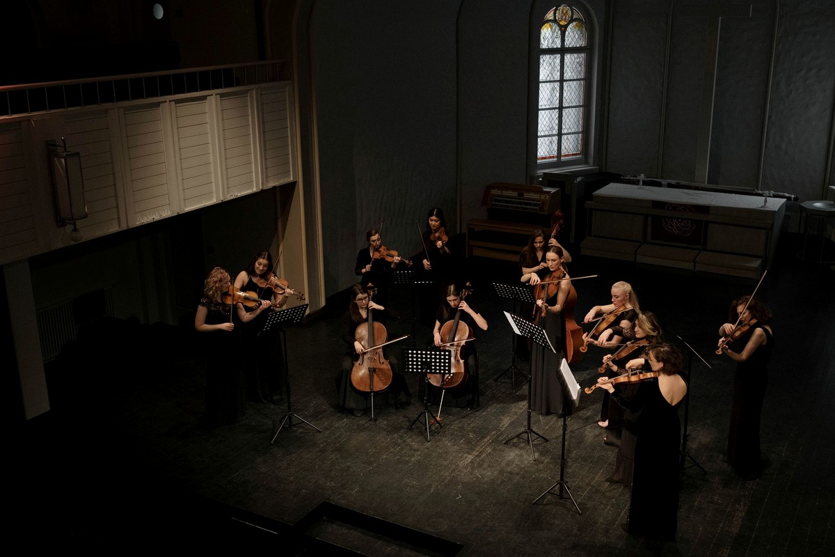 Wooden dock in the evening with a small stage built, brass instrument stands and festoon lighting over the floor.
