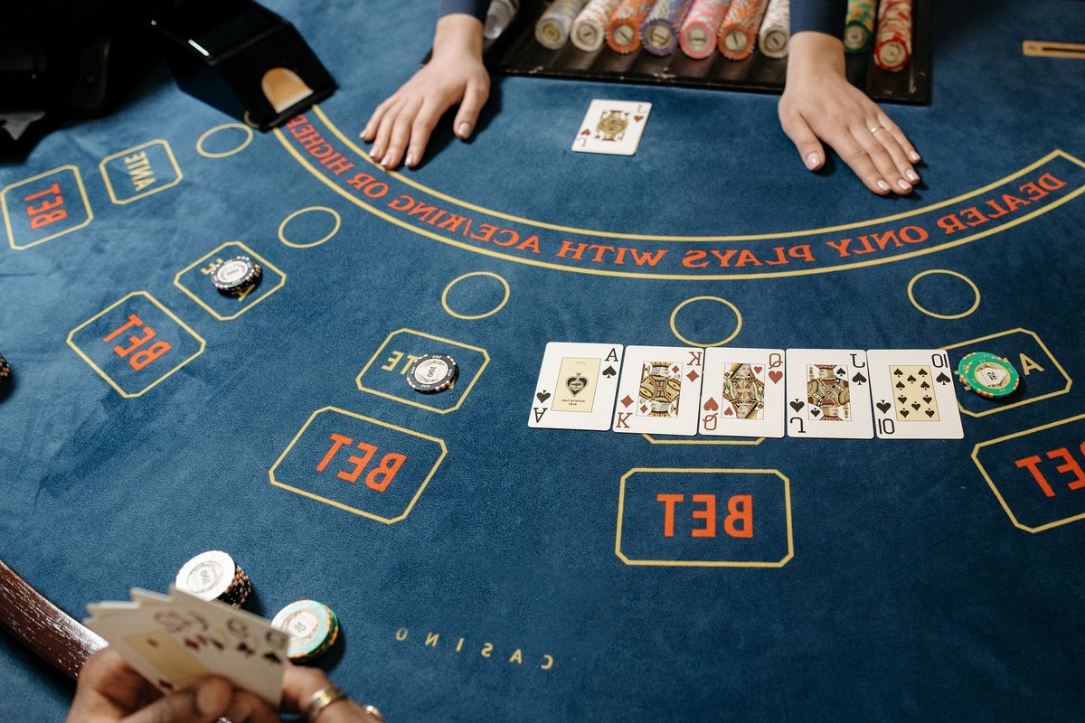 Table nappée de feutre vue de côté, jetons empilés en trois piles, mains d'un croupier en gilet au-dessus du tapis.